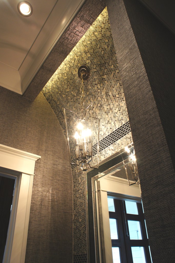 This picture shows the different curves and lines, as well as the palette of textures I used in the Powder Bathroom.  The walls are a blue-gray grasscloth.  The main tile on the vanity wall is a glass herringbone mosaic tile, separated by bands of smoky mirror staggered tiles.