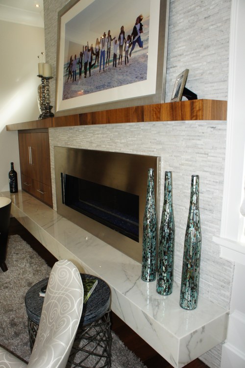 The fireplace surround is covered in horizontal pieces of Carrera marble with varying depths and alternating polished and tumbled finishes.  The hearth is made from slabs of Carrera marble.  This white helped balance all the wood tones in the room.
