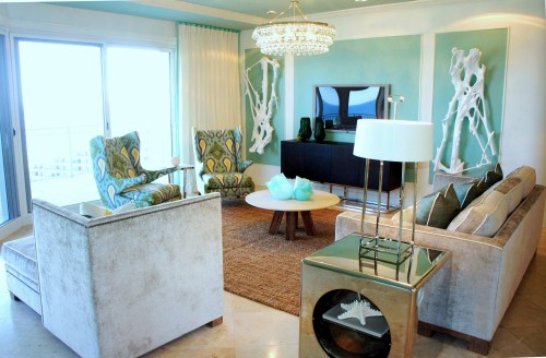 One great way to decorate a large, intimidating blank wall is to create the illusion of wall panels with simple wood trim pieces.  Then, you can add a contrasting color or pattern to the center-here I painted them a rich aqua color! The panels not only break up the wall; they also frame the driftwood sculptures and help to liven up the focal wall! The glass chandelier adds some bling to the room, and mimics the round cocktail below it.