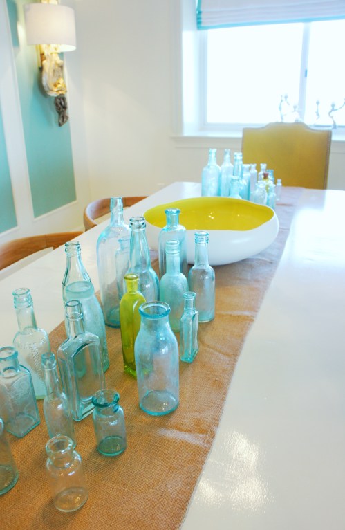 For my centerpiece, like many other details in this condo, I decided to go big or go home!  For a vibrant color pop, I found a lot of antique glass bottles and congregated them on my burlap table runner.  When entertaining, these bottles would look beautiful with the occasional daisy , and the bowl would look great with floating candles!