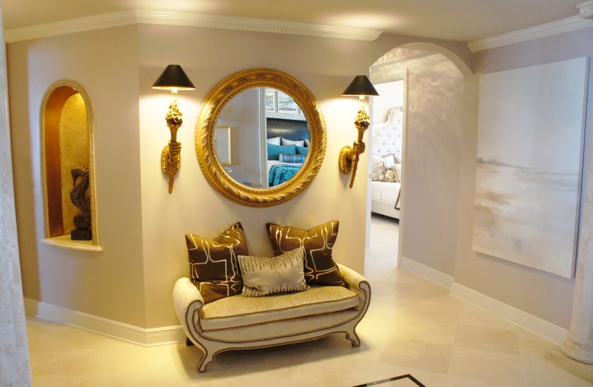 I brightened this hallway up with a new paint color and some plush seating!  The sconces were hung at an odd height, so I lowered them to a more balanced position.  I gold-leafed the inside of the wall niche for some added glowing warmth, then hung a light, but rich canvas painting on the wall to the right.  This painting kept the feeling light, but still rich.  The owner of this unit is a lamp and lighting designer, so I thought this brown and gold lamp fabric was just perfect!!