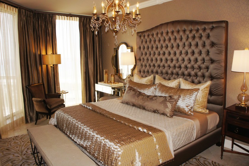Master Bedroom After: Having started with quite the blank slate, I began my design of this room with a subtle printed wallcovering on the bed wall.  I painted the walls taupe, like the background of the wallpaper.  I covered the grand, tall custom headboard in the same taupe taffeta as the drapes.  The gold striped sheers add a subtle gauzy layer of warmth to the room. The lines of the new chandelier emulate the ribbon-work pattern of the wallpaper.  