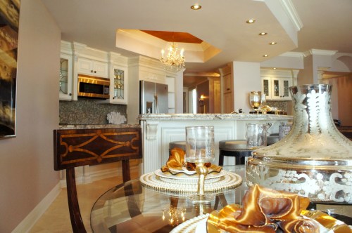 Here you can see the dramatic change in the kitchen! In the upper cabinets, the glass shelves and mirrored backs help open them up and add depth.  The strange placement of gold paint on the inside of the ceiling tray was replaced with an extension of the new ceiling color.  The crown was painted off-white, and I added a gold shimmering grasscloth to the ceiling, inside the recessed tray.  This provided drama and emphasis to this ceiling treatment, but in a more natural, aesthetically-pleasing way. 