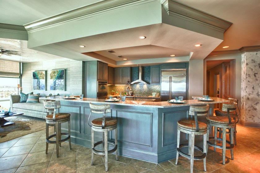 In this kitchen makeover, we provided new countertops, finished the cabinets in a distressed warm gray, added some paneling to the bar front and livened the backsplash with new tile.
